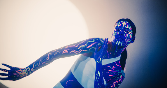 Young Dancer Delivers Captivating Improvised Contemporary Dance Performance, Adorned in Vibrant Neon Body Paint and White Clothes, Against an Abstract Art Background in a Dark Space