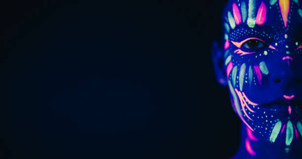 istock Innovative Beauty Advertising Shoot: Talented Model Showcases Her Unique Style, Neon-Painted Body and Face Contrasting Beautifully with Dark Backdrop, Creating a Visually Stunning Close Up Portrait 1530710577