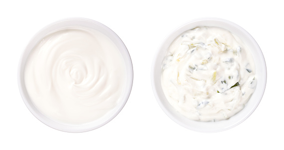 Cream yogurt and tzatziki, in white bowls. Stirred cream yoghurt with high fat content. Pure (left side), and as Greek dip sauce, mixed with cucumber, garlic, salt, olive oil and herbs (right side).