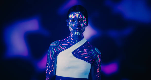 istock Innovative Beauty Advertising Shoot: Talented Model Showcases Her Unique Style, Neon-Painted Body and Face Contrasting Beautifully with Dark Abstract Backdrop, Creating a Visually Stunning Image 1530722819