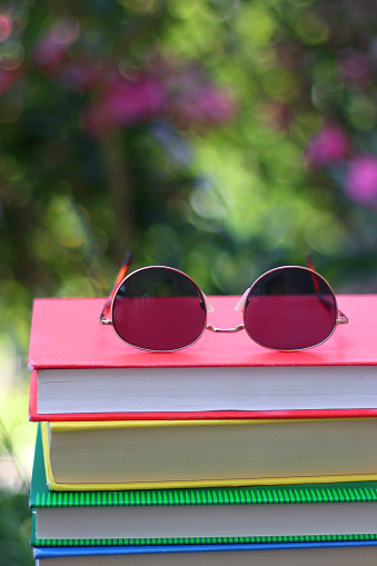 Stack of colorful hardcover books and sunglasses in the garden. Summer reading concept. Selectvie focus, colorful background.
