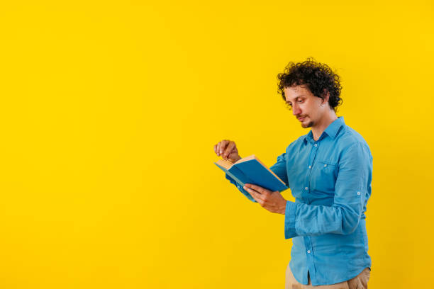 istock Young Man Reading A Book In Front Of A Yellow Wall 1530776284