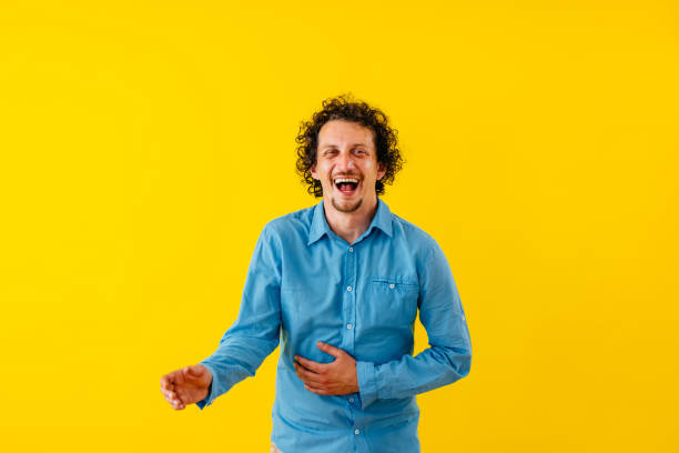 Portrait of a handsome young man laughing while standing in front of a bright yellow wall.