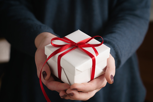 young female hands holding gift box with red ribbon, shallow focus