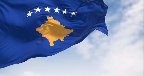 National flag of Kosovo waving in the wind on a clear day. Blue with a yellow map of Kosovo and six white stars above it. 3d illustration render, Fluttering fabric.