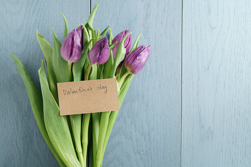 bouquet of purple tulips on blue wood table with paper card for valentines day, top view