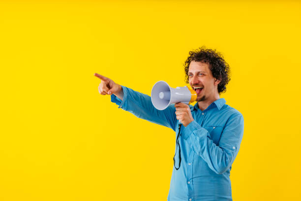 istock Young Man Talking Into The Megaphone In Front Of A Yellow Wall 1530778705