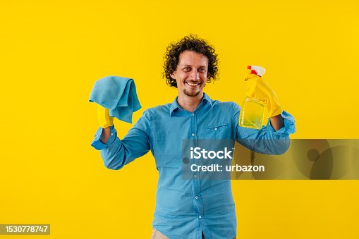 istock Happy Young Man Holding Spray Bottle And A Cloth In Front Of A Yellow Wall 1530778747