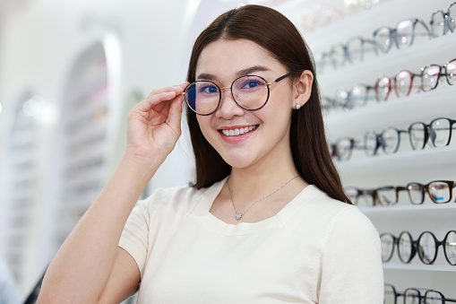 Beautiful young woman choosing eyeglasses frame in an optical store.