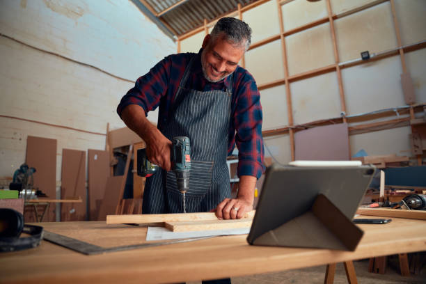 istock Mid adult man smiling while using drill on timber next to digital tablet in woodworking factory 1530778848