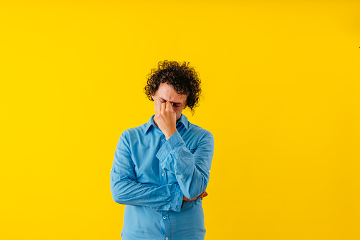 Portrait of a sad young man standing in front of a yellow wall.