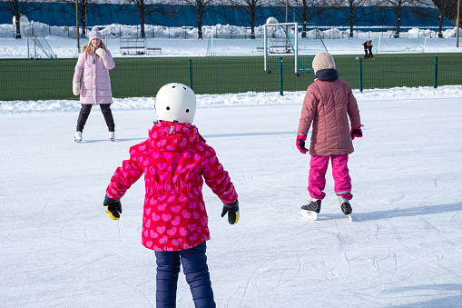 Two Caucasian girls, 7 years old, are training, skating. A woman trains children to stand on skates correctly.