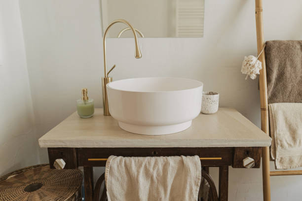istock Modern bathroom interior. Modern ceramic sink with golden faucet on rustic stand with soap and ladder with towel on background of wall with mirror. Stylish boho bathroom design. 1530782646