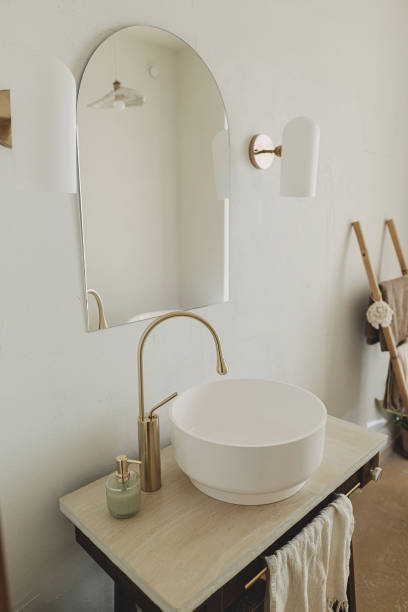 istock Modern bathroom interior. Modern ceramic sink with golden faucet on rustic stand with soap and towel on background of wall with mirror and travertine tile. Stylish boho bathroom design. 1530784251