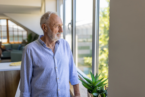 Portrait of a senior Caucasian man looking out a window at home