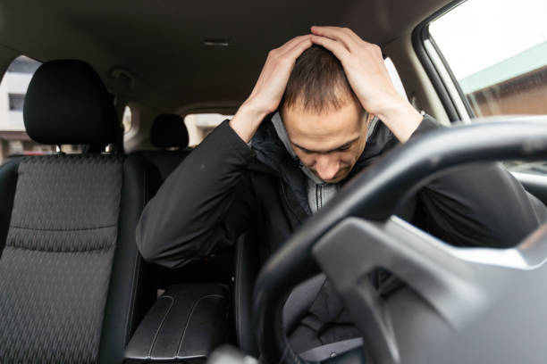Young bearded business man sitting in car very upset and stressed after hard failure and moving in traffic jam stock photo