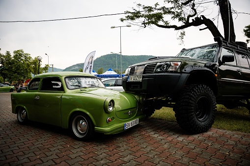 Targu Ocna, Romania – June 23, 2023: A large black car parked halfway on top of a vintage green car at a Tuning Show