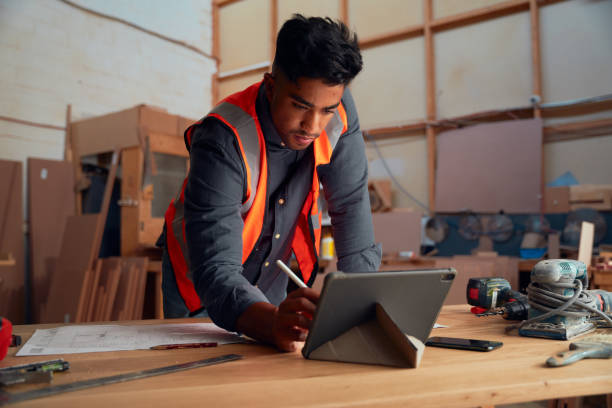 istock Young man in reflective clothing writing with digitized pen on digital tablet in woodworking factory 1530808444