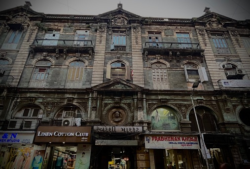 Mumbai, India – February 18, 2022: A group of people are walking past a vintage building with several broken windows