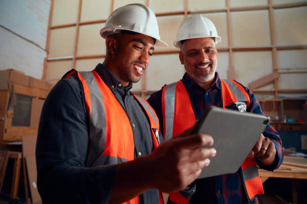 istock Men in reflective vest and safety helmet smiling while looking at digital tablet in woodworking factory 1530810217