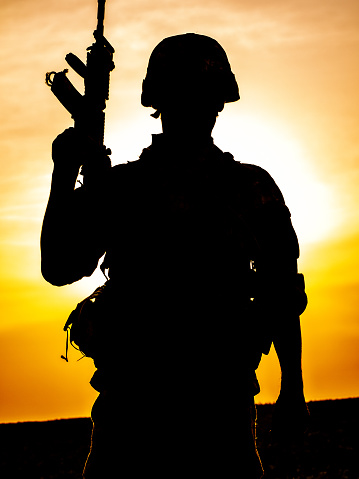 Silhouette of US soldier with rifle at sunset standing as the sun sets in the background