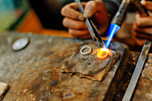 Man holding welding torch melting the silver rings