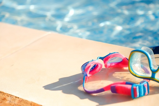 A close-up of two swimming goggles placed on the edge of the pool