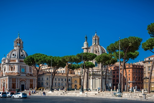 Piazza Venezia Charm: Bustling scene with Santa Maria of Loreto and Holy Name of Mary churches, traffic, pedestrians, curved roof buildings and trees
