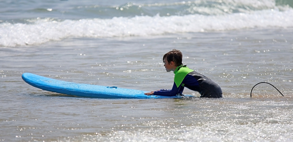 A boy in a neoprene wet suit and surfboard entering the water to surf