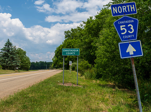 The State Route 53 North sign in front of the Chautauqua County sign in Carroll, New York, USA on a sunny summer day