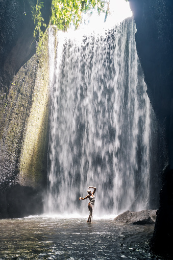 Woman enjoying sunrise at the beautiful waterfall on Bali island in Indonesia