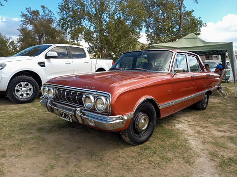 Chascomus, Argentina – April 16, 2023: Old red maroon Ford Falcon Deluxe sedan 1970 - 1972 on the lawn. Nature, grass, trees. CAACMACH 2023 classic car show