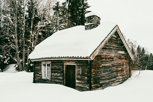 A rustic wooden cabin covered in a blanket of fresh snow in the stunning landscape of Lake Mjosa, Norway