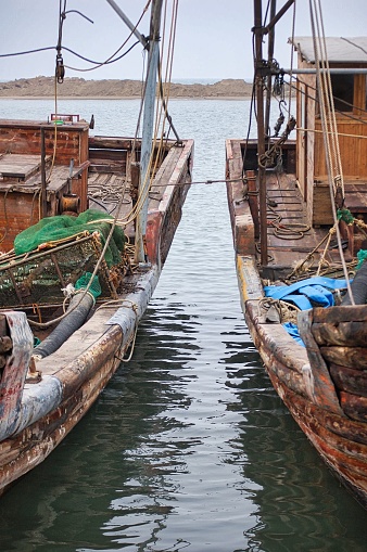 Two traditional fishing vessels, securely moored to a dock, situated side-by-side in a tranquil body of water