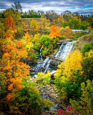 An autumn landscape featuring vibrant foliage, cascading waterfalls, and moody gray clouds