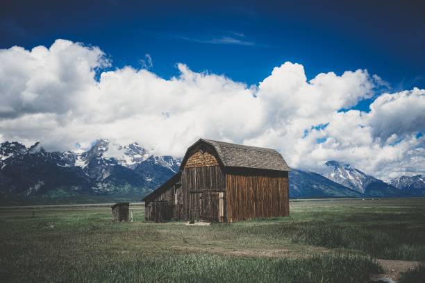 istock a rustic barn in an open field near mountains and clouds 1530898975