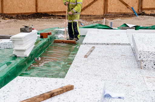 Builder placing polystyrene insulation boards on waterproofing membrane during floor construction. Energy saving concept