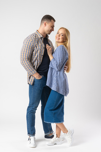 Man and woman hugging while looking at the camera. Young married couple in casual clothes. Models posing on white background