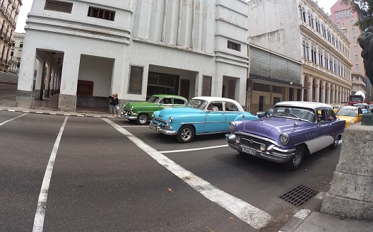 Havana, Cuba – March 15, 2017: A row of vintage cars parked along a city street next to an urban building in Havana