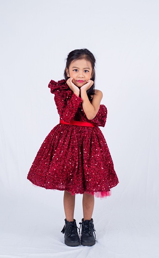 A young girl in a glittery red dress and black boots posing on the white background