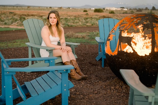 A female adult sitting on a comfortable outdoor chair next to a roaring fire pit