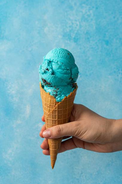 istock Hand holding two scoops of blue ice cream cone against a blue background 1530920494