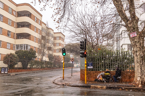 Street beggars huddling during the snow blizzard in Johannesburg, Killarney, with an old retro apartment block, July 10, 2023.