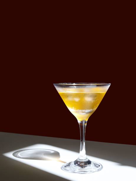 Clear glass filled with a light-colored drink sits atop a white table in a brightly lit room