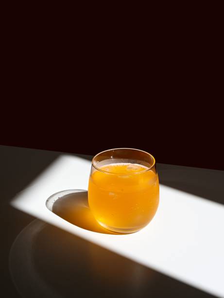 Clear glass filled with a light-colored drink sits atop a white table in a brightly lit room