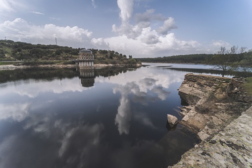 Photograph representing the El Villar reservoir in which we can see the water and how the architecture and clouds are reflected above it.