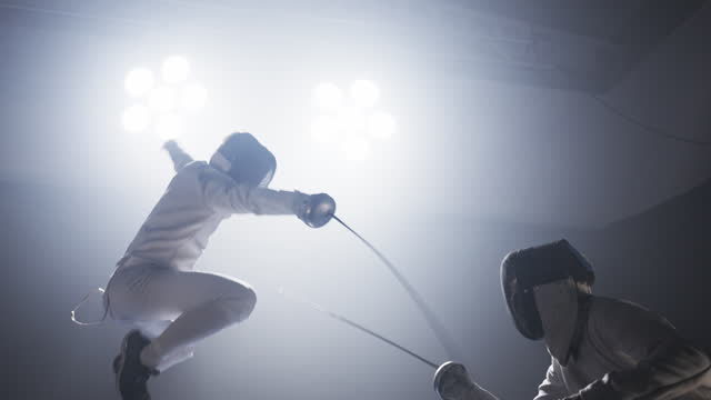 Two professional fencers in full protective gear clashing foil sabers in a match. Lunging and hitting