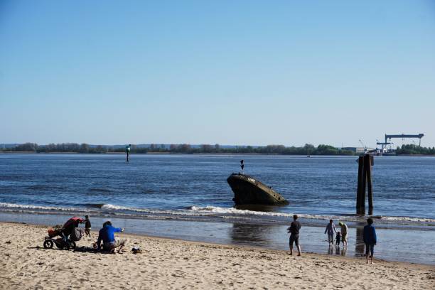 Familiy scenes at the beach with blue sky, ship wreck, industrial site in the background Hamburg, Germany – April 30, 2023: Familiy scenes at the beach with blue sky, ship wreck, industrial site in the background along Elbstrand in Hamburg övelgönne stock pictures, royalty-free photos & images