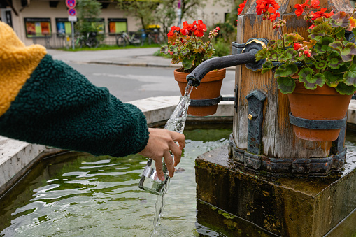 A close up of an unrecognisable man in Garmisch in south Germany. He has stopped at a water fountain in the town centre which provides the town with flowing free spring water from the mountains, He is filling up his reusable glass bottle.