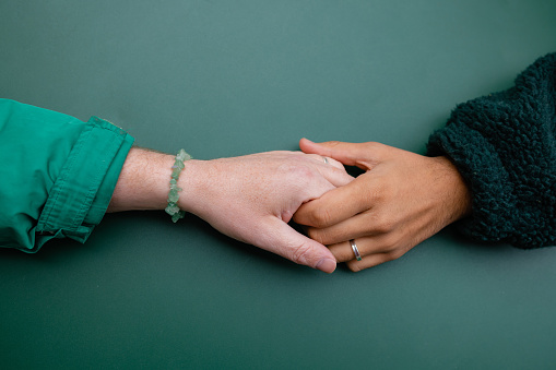 A close up aerial view of a gay couple holding hands across a table a cafe in Germany. They are on holiday and are wearing their engagement rings on their fingers.